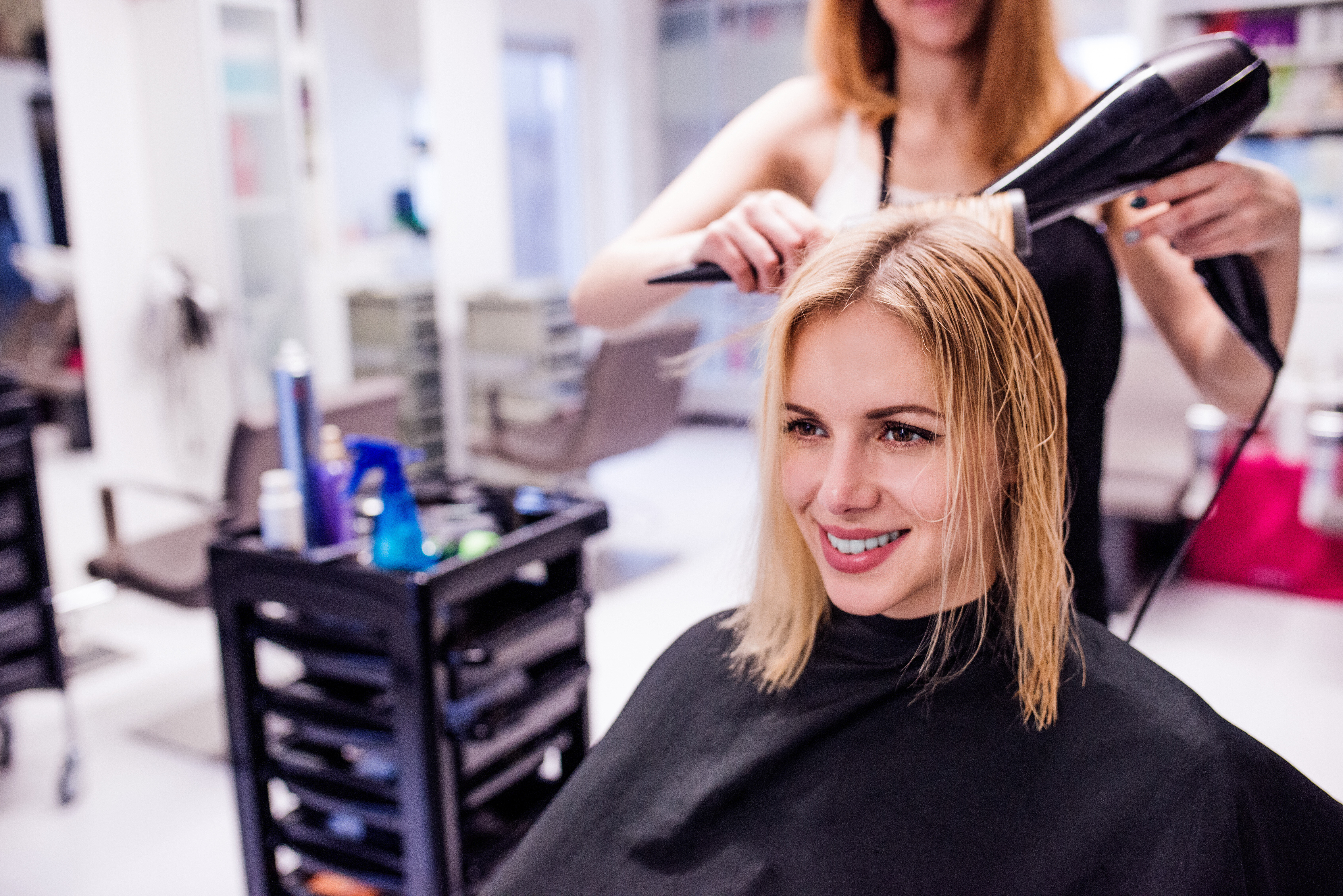 A hairdresser blow-dries a client’s mid-length hair