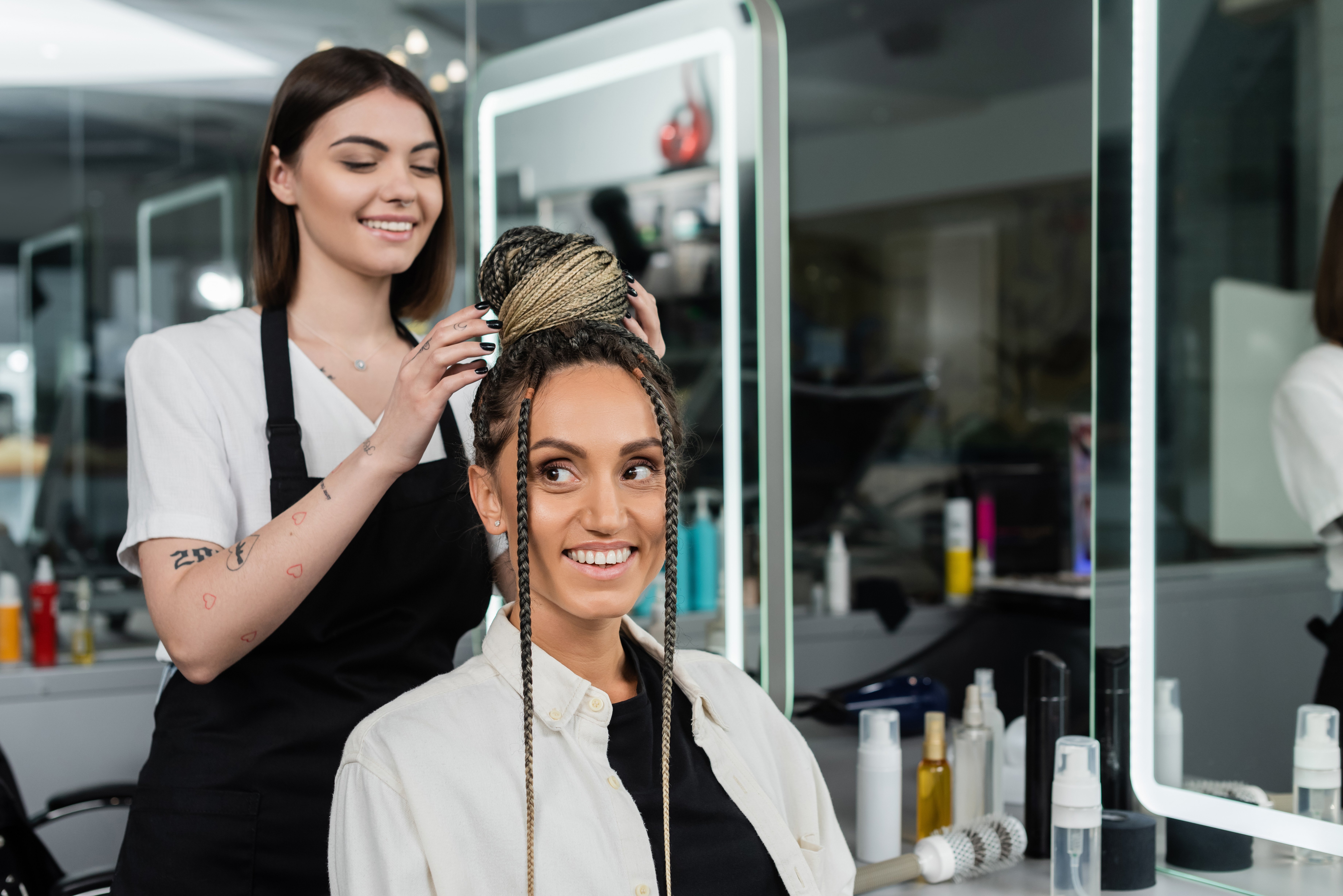 A hairdresser in a salon does a braid hairstyle for an excited client