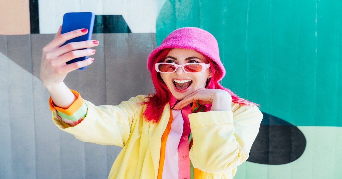 A woman with pink hair captures a selfie.