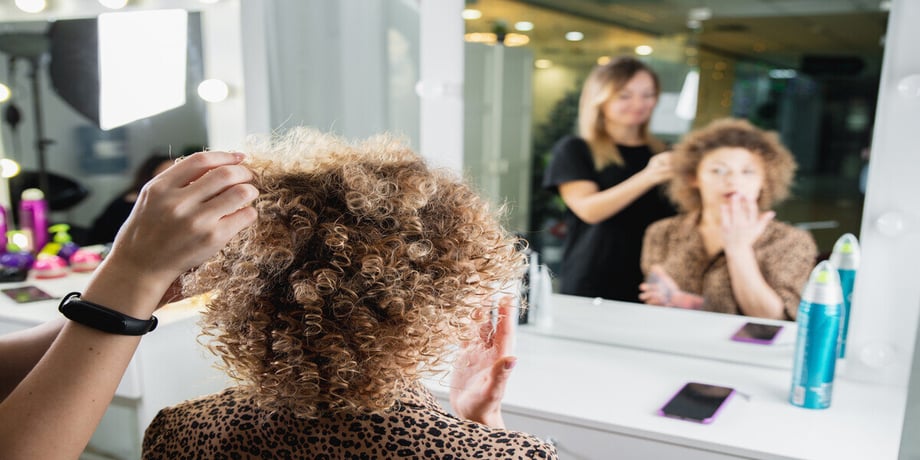 A woman in the salon looks in the mirror while a stylist styles her.