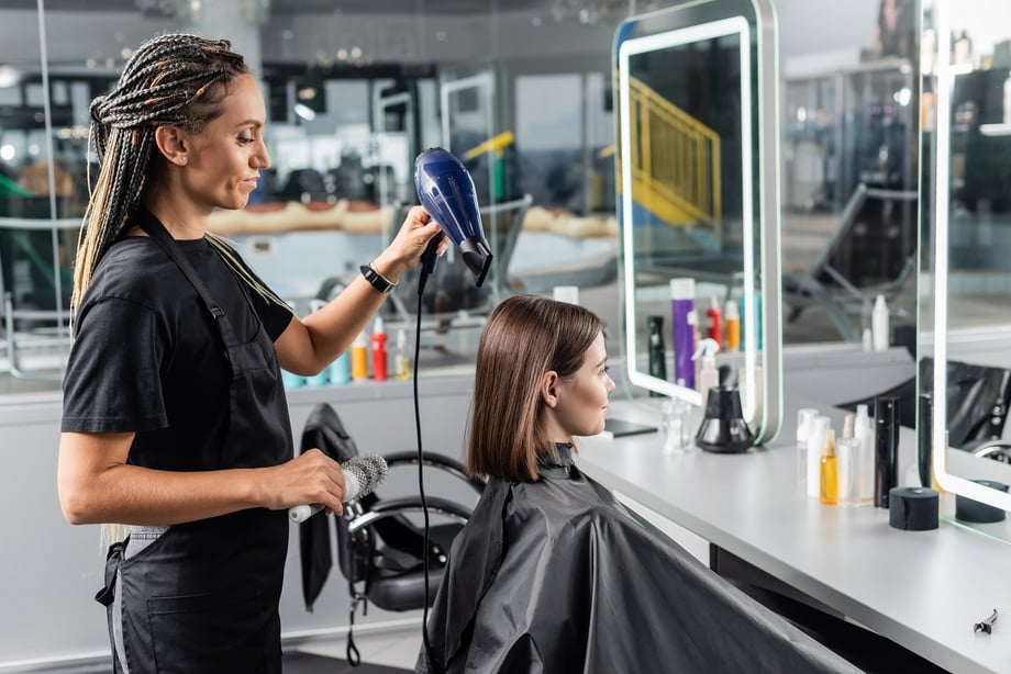 Hairstylist using a hair dryer on a customer's hair in a salon setting.