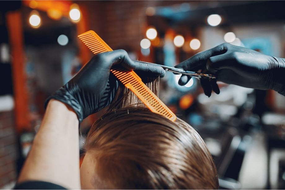 A stylist cuts the hair of the person that sits in front of him. 