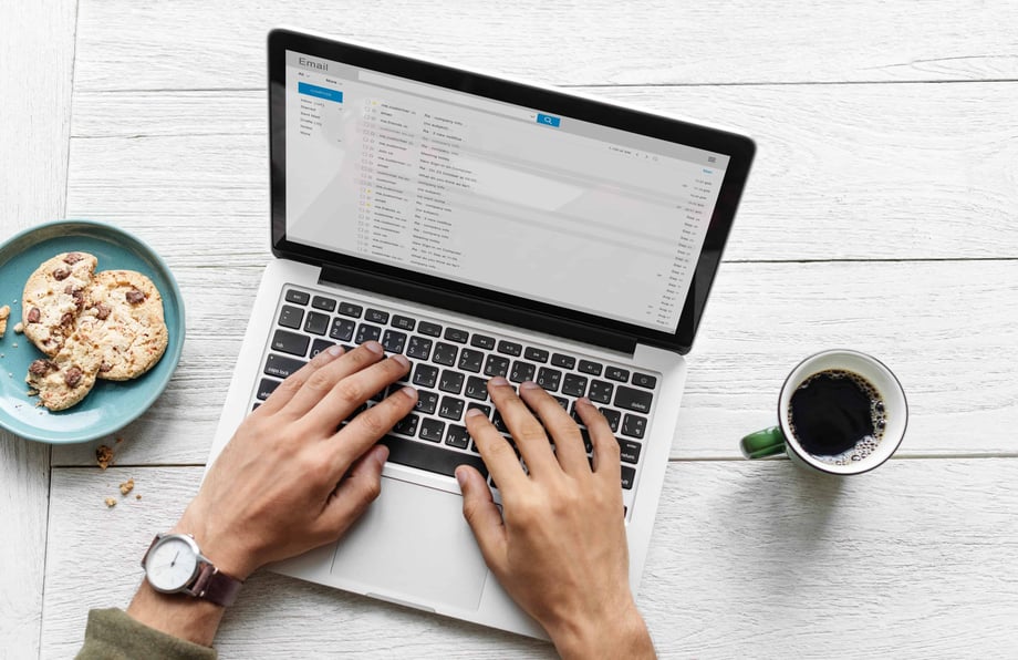 Person typing on computer with cookies and coffee on the table