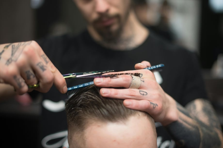 A man cuts the hair of the person sitting in front of him. 