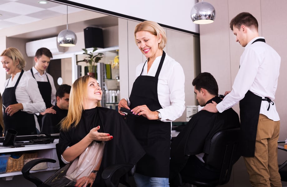 Two hairdressers interact with clients in a unisex salon.